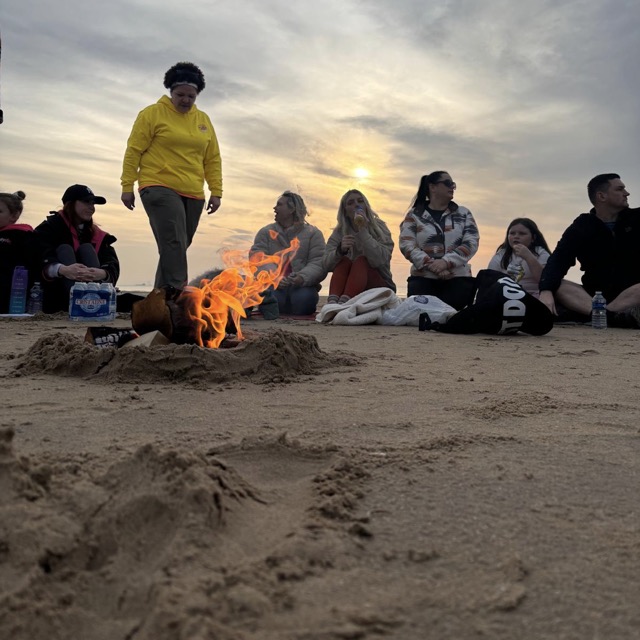 A small beach fire with the group sitting around it at sunset.