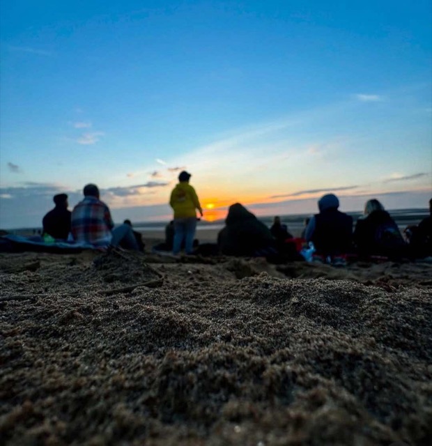People sitting on a beach watching the sun set over the sea.