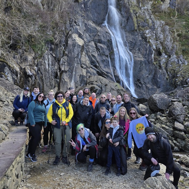 A Nature Awareness group gathered at the foot of a waterfall on a bright spring day.